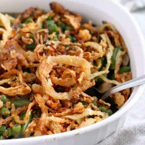 Green bean casserole topped with crispy onions in a white oval dish.
