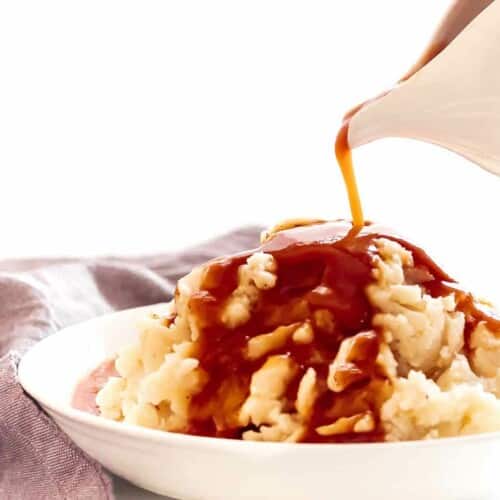 Gravy pouring from a pitcher onto a bowl of mashed potatoes.