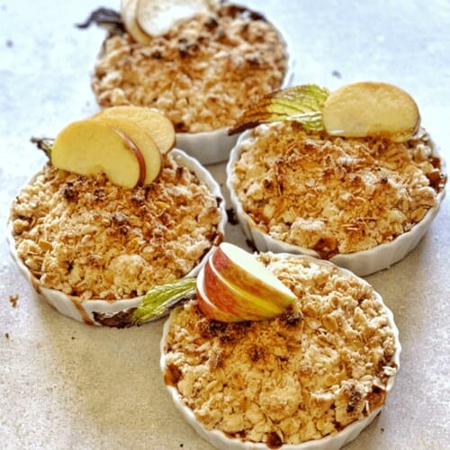 Four apple crumb desserts on the table garnished with fresh apple slices.