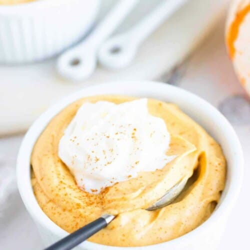 Pumpkin pudding in a white ramekin with whipped cream on top.