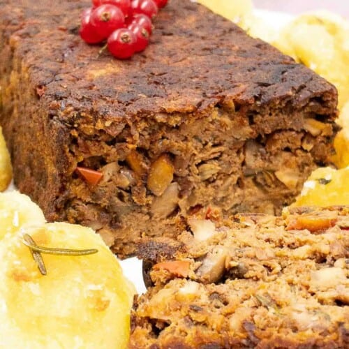 Vegan meatloaf sliced on a plate with potatoes and red berries for garnish.