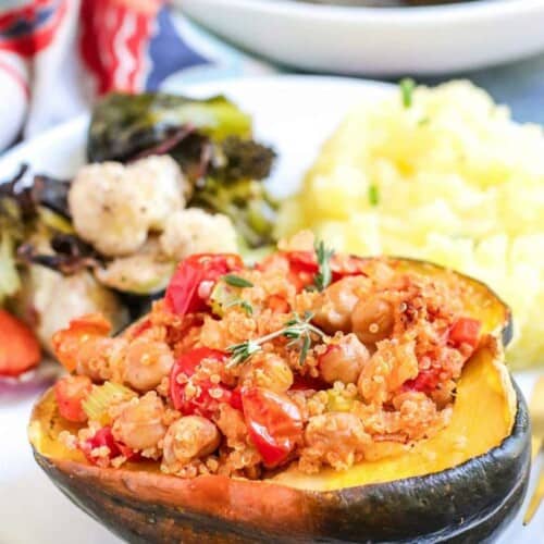 Stuffed acorn squash on a plate with mashed potatoes and vegetables.