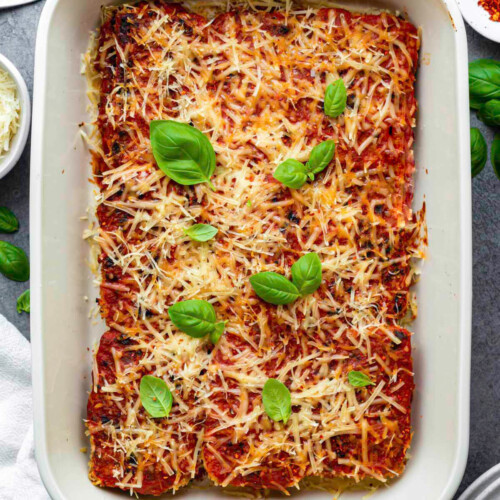 A white baking dish serve with vegan tofu parmesan and topped with fresh basil leaves.