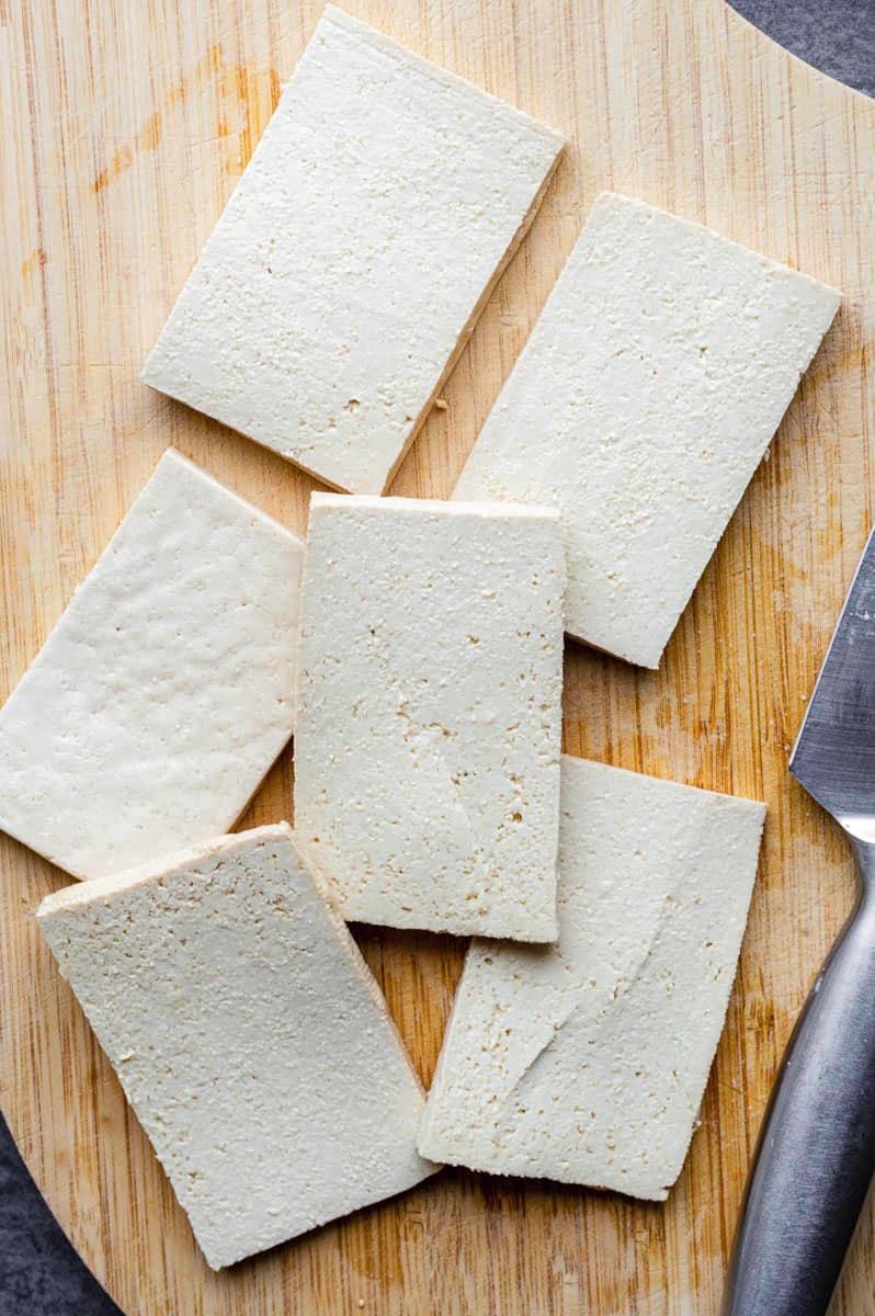 Slices of tofu on a wooden cutting board.