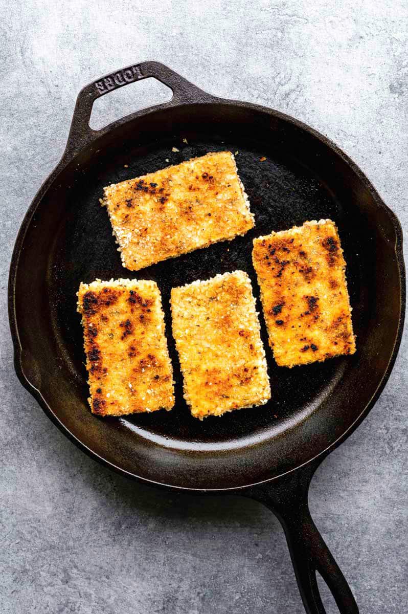 Frying four pieces of breaded tofu in a cast-iron skillet.