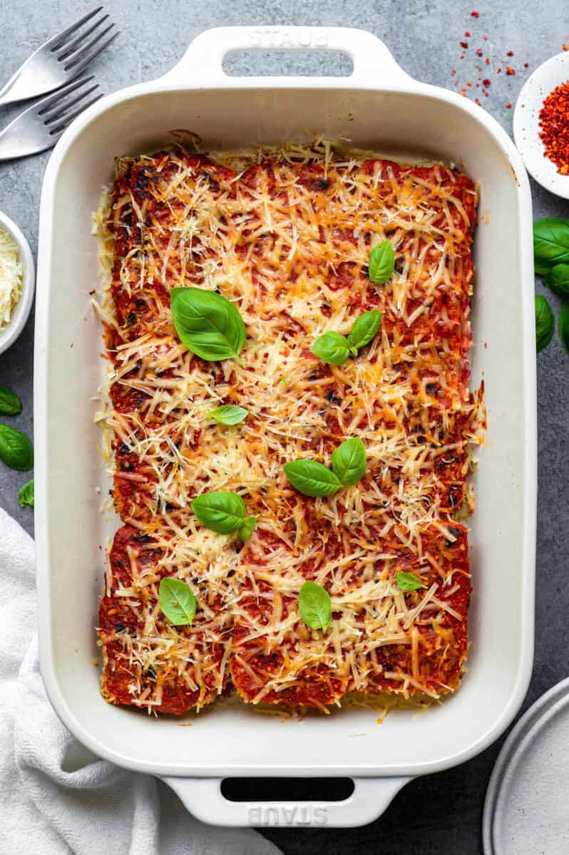 A white baking dish serve with vegan tofu parmesan and topped with fresh basil leaves.