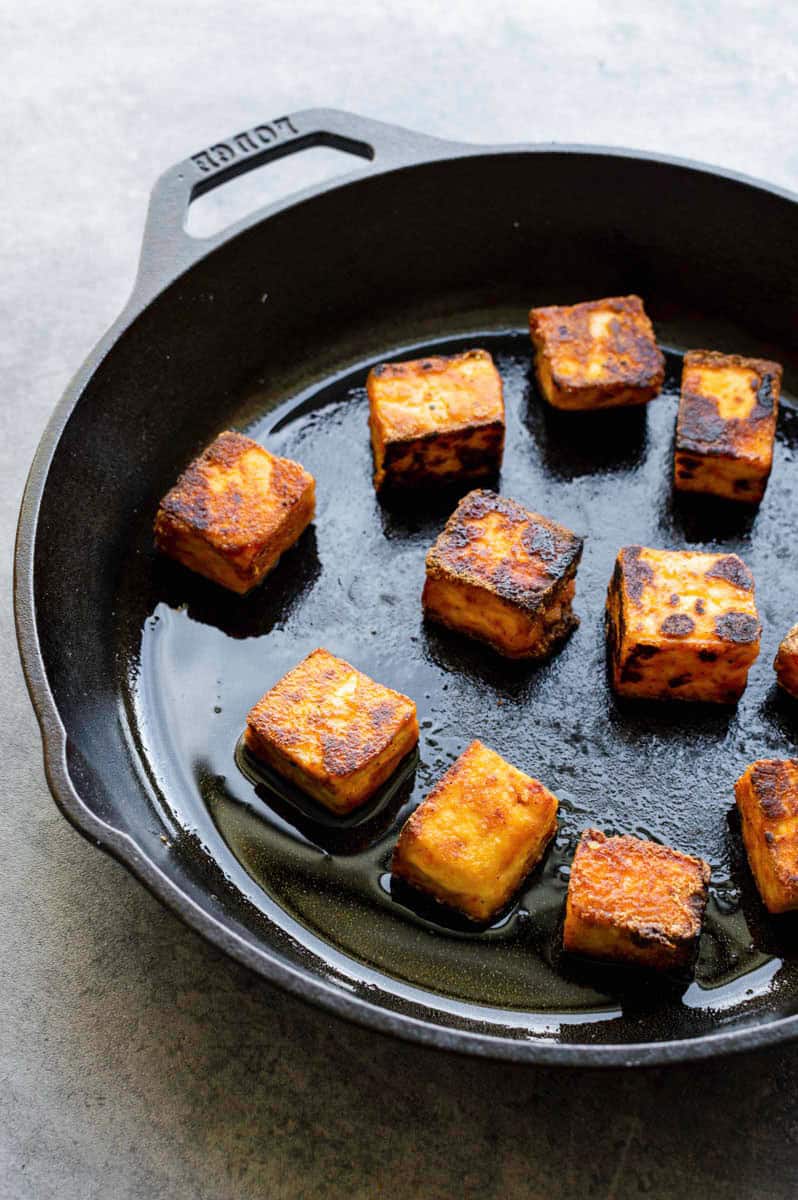 Frying tofu cubes in a cast-iron pan.