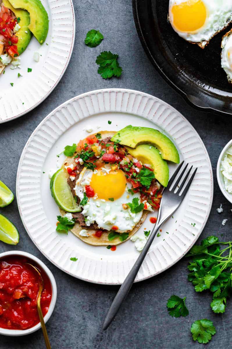 Vegetarian Huevos Rancheros served on a white plate and topped with feta cheese, avocado, and fresh cilantro.