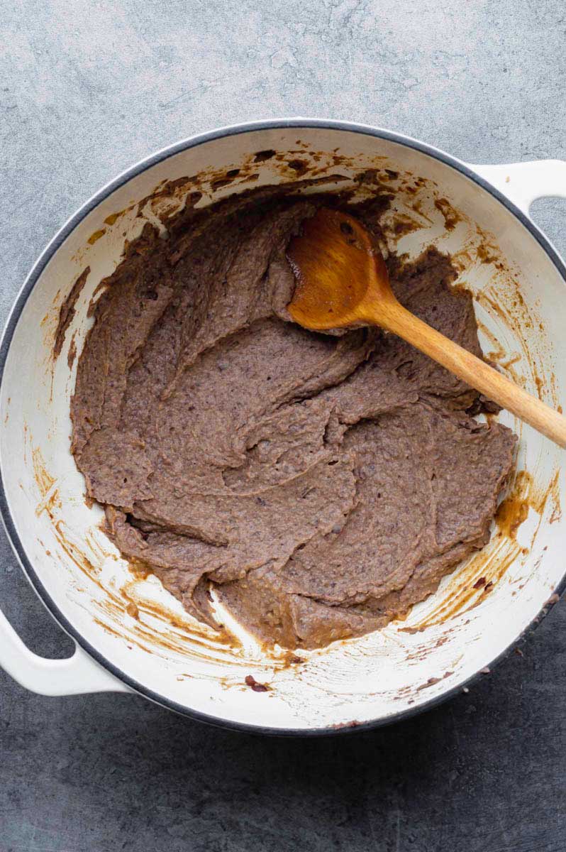 Refried beans in a white Dutch oven with a wooden spoon placed in it.