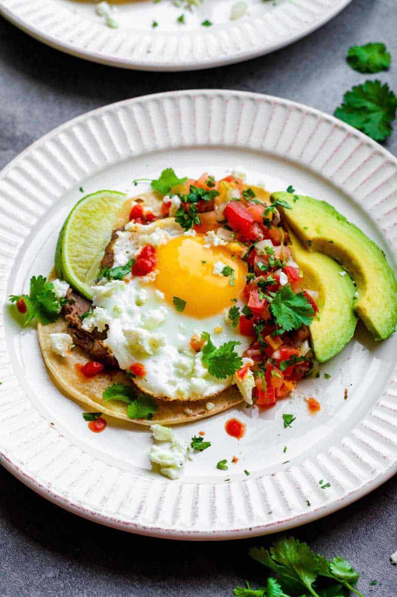 Vegetarian huevos rancheros served in a white plate garnished with pico de gallo, avocado and a lime wedge on the side.