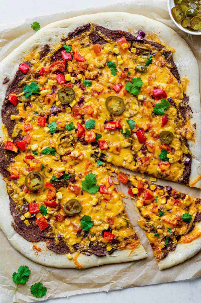 Vegetarian mexican pizza on a piece of brown parchment paper.  The pizza is topped with fresh coriander and pickled jalapenos.