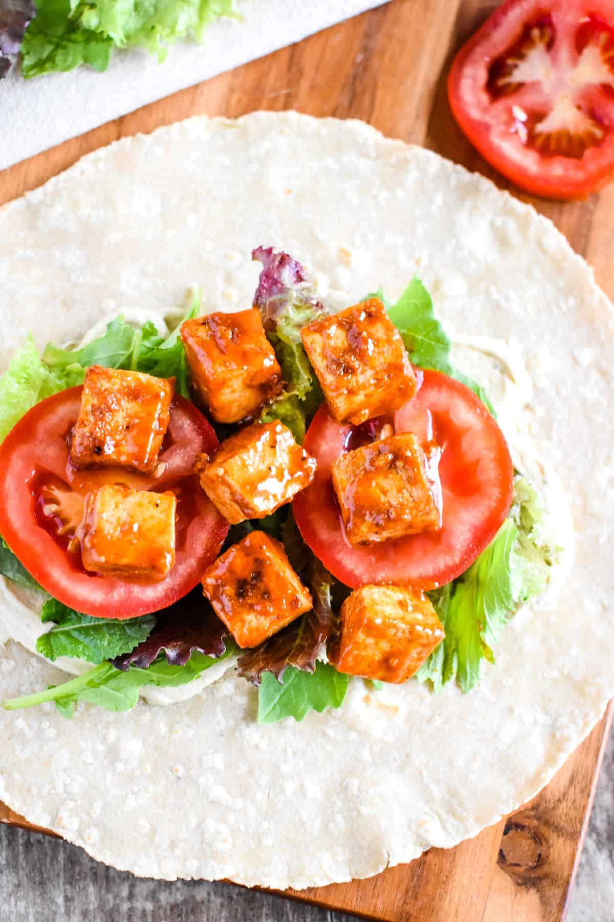 tofu in a wrap with hummus, greens and tomatoes.