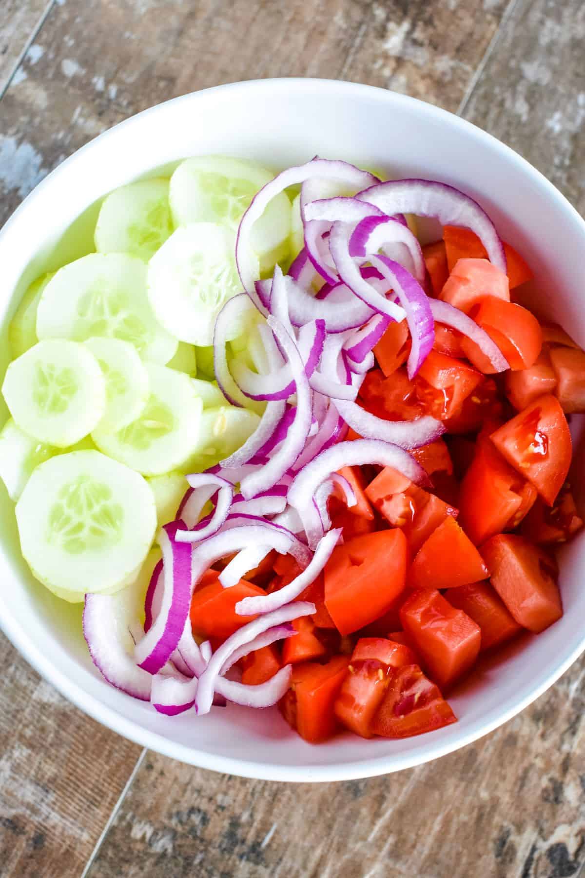 tomatoes, onion and cucumbers added to a mixing bowl.