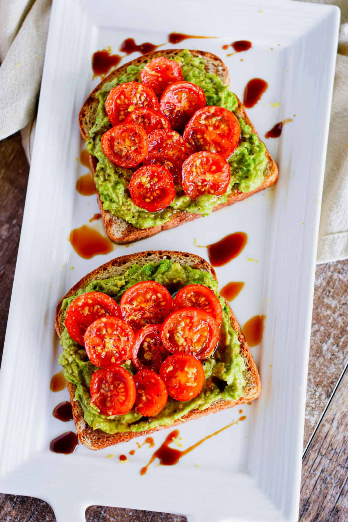 overhead of two slices of tomato avocado toast on white serving dish.