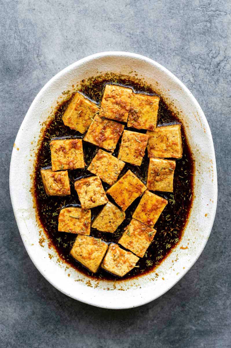 Overhead of tofu being marinated in a shallow white dish.