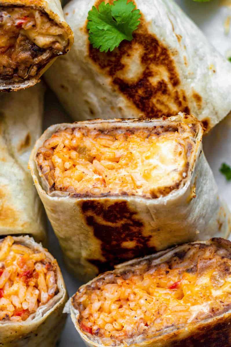 A close-up photo of a half of a burrito filled with rice, beans, and cheese sauce.