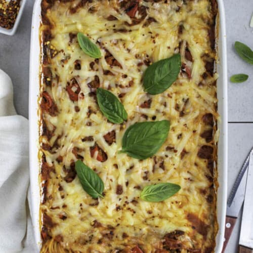 Vegan baked spaghetti in a white casserole topped with fresh basil leaves.
