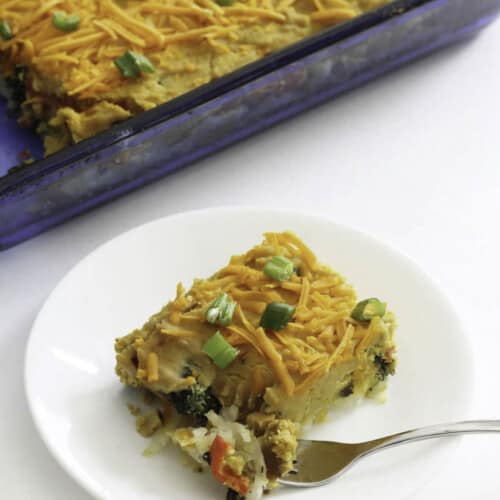 A piece of vegan breakfast casserole served on plate with casserole in background.