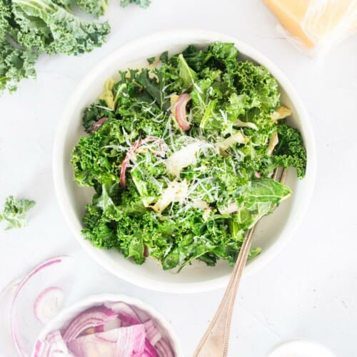 overhead of warm kale salad in a white bowl with a fork in it.