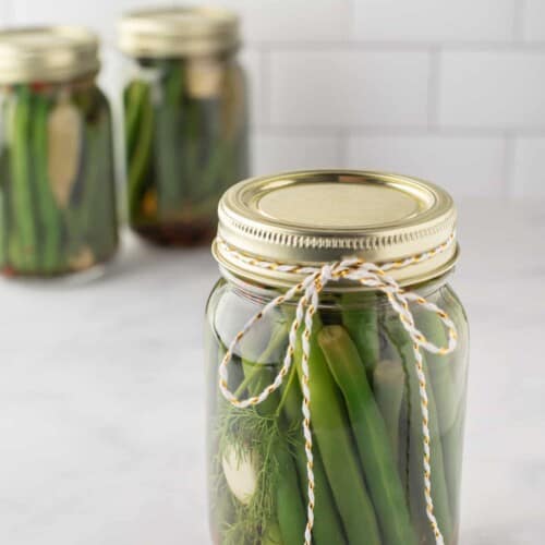 Pickled green beans in a mason jar with two more jars in the background.
