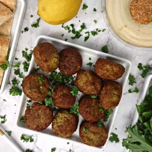 overhed of falafel on a square plate with garnish around.