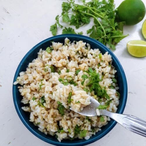 sobrecarga de arroz integral con cilantro en un tazón con un tenedor sosteniendo un poco.