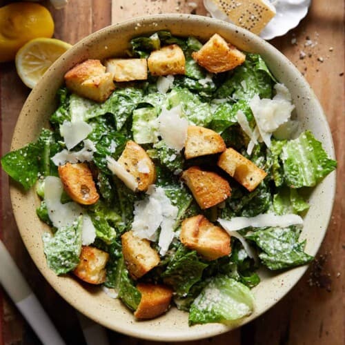 overhead of caesar salad in a bowl on a wooden surface.