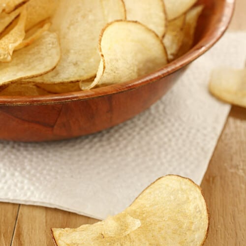 homemade potato chips in a wooden bowl with some on the table.