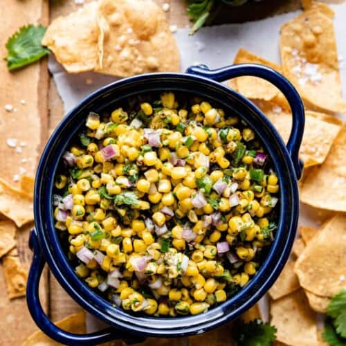 overhead of corn salsa in a blue serving bowl with tortilla chips around it.