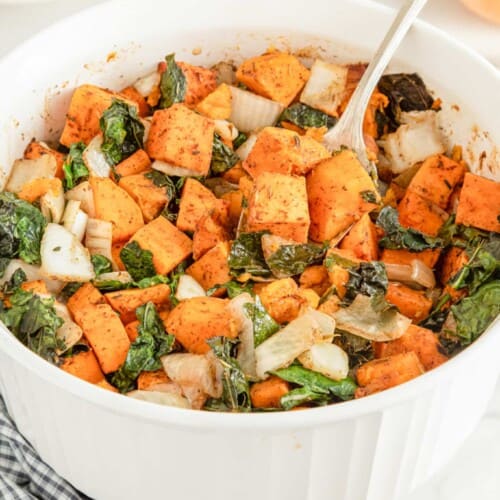 sweet potato kale casserole in a white serving bowl with a spoon in it.