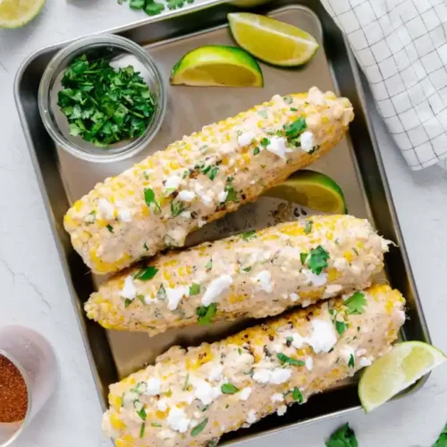 vegan Elote on a tray with coriander and lime wedges around it.