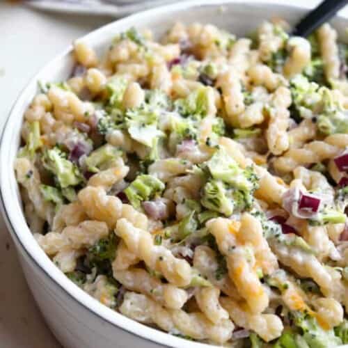 close-up of broccoli pasta salad in a white bowl with a spoon in it.