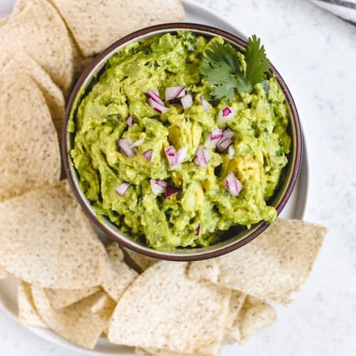 overhead of fresh guacamole in a bowl with tortilla chips surrounding it on a plate.