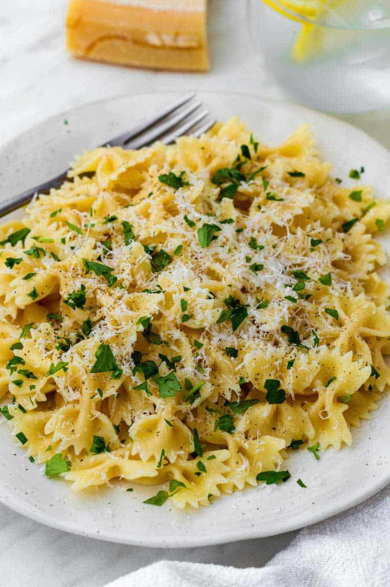 A white plate filled with pasta topped with parmesan cheese and fresh chopped parsley.