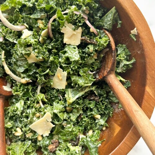overhead of tahini kale salad in a wooden bowl with a wooden serving spoon in it.