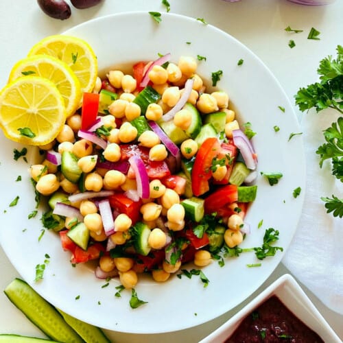 overhead of mediterranean chickpea salad in a white bowl with lemon and parsley garnish.