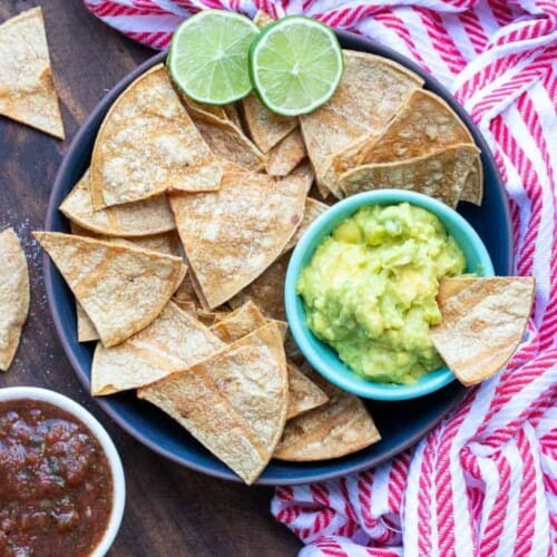 overhead of baked tortilla chips in a bowl with a side of guacamole in the bowl.