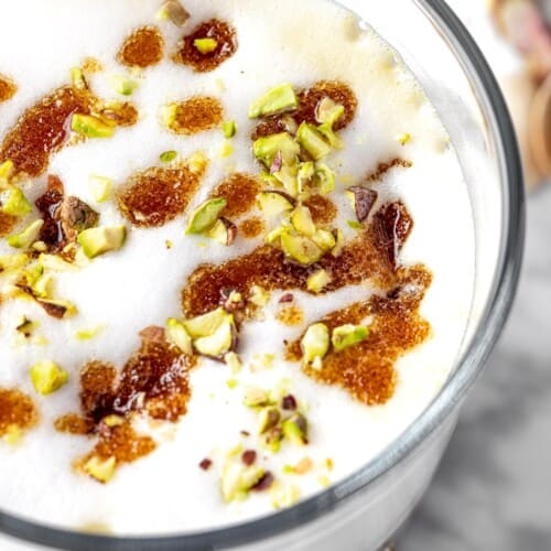 latte in a glass with pistachio pieces on top.