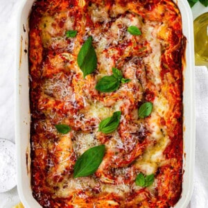 Three cheese lasagna in a ceramic baking dish topped with grated parmesan cheese and basil leaves.