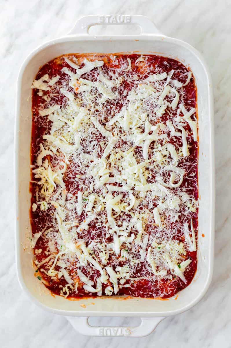 Uncooked lasagna in a ceramic baking dish topped with shredded mozzarella and parmesan cheese.