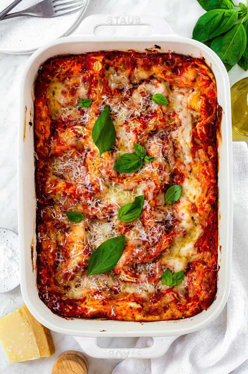 Three cheese lasagna in a ceramic baking dish topped with grated parmesan cheese and basil leaves.