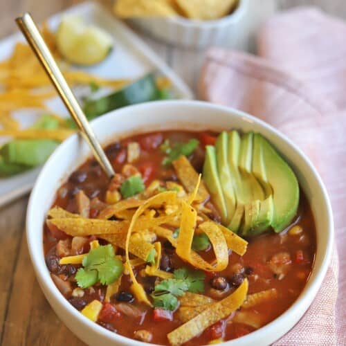 vegan tortilla soup in a white bowl with a spoon in it.