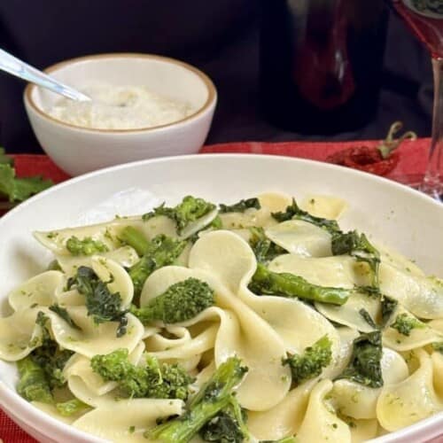 serving of rapini pasta in a white dish on a red kitchen towel.