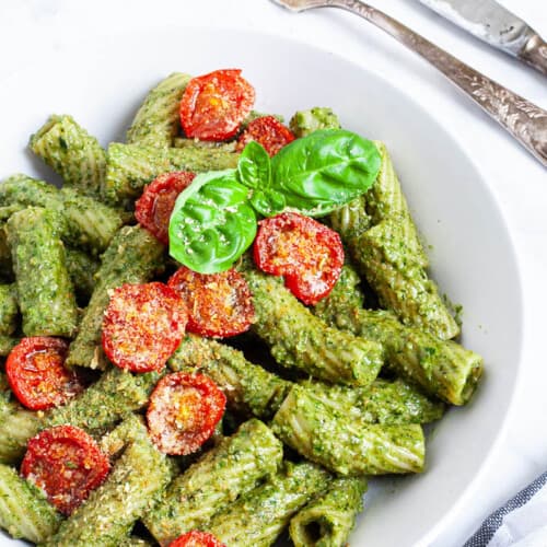 close-up of pesto pasta with cherry tomatoes in a white bowl.