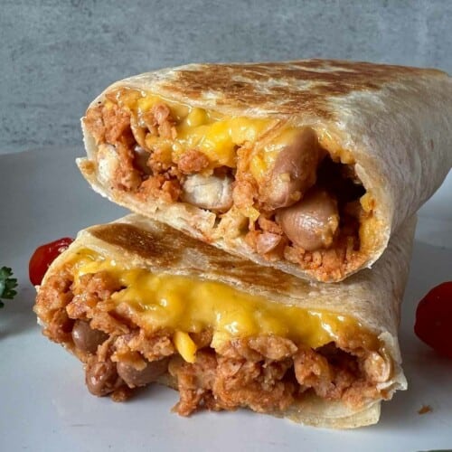 Two burritos cut in half and stacked on top of each other. They're served on a white plate.