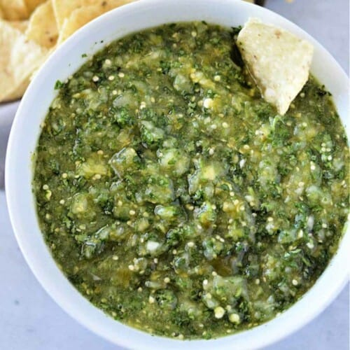 Salsa verde served in a white bowl and garnished with tortilla chips.