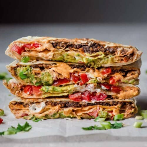 Four vegan crunchwrap supremes stacked on top of each other and placed on a piece of prachment paper.