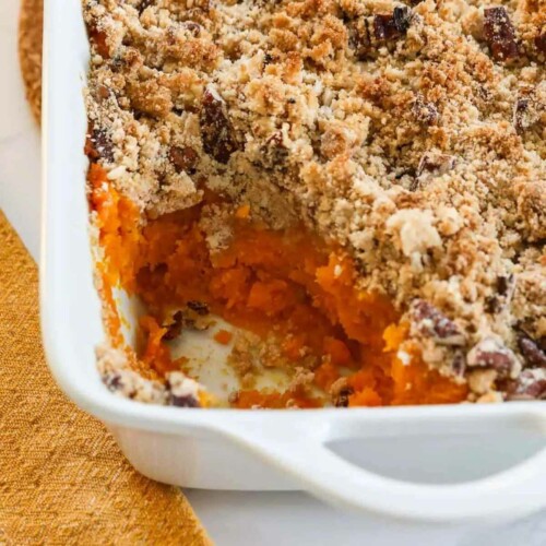 Sweet potato casserole in a white casserole dish. A kitchen towel placed next to the casserole.