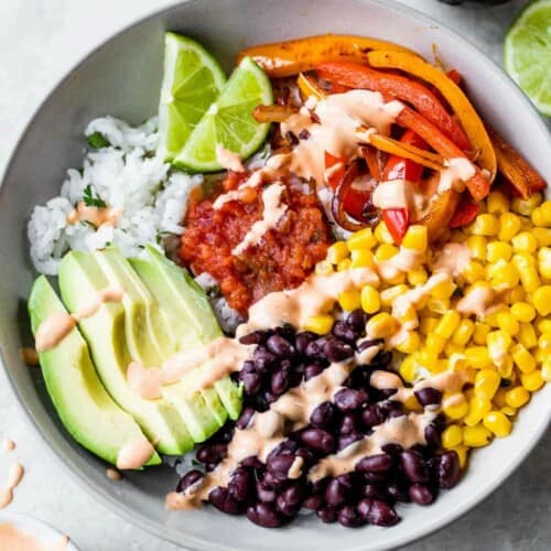 A bowl of rice topped with black beans, corn, peppers, avocado, salsa, and chipotle aioli.