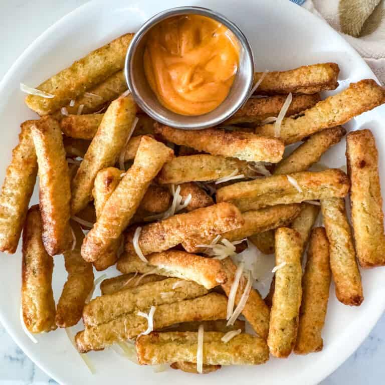 Air Fryer Frozen Zucchini Fries feature image 1200x1200. Fries set on a white plate served with chipotle sauce and garnished with parmesan cheese